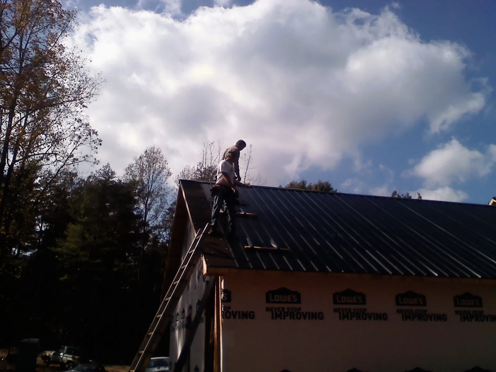 Roofer fastening dark metal panels high against a cloudy sky, from a Roof Inspection job in Greenwich