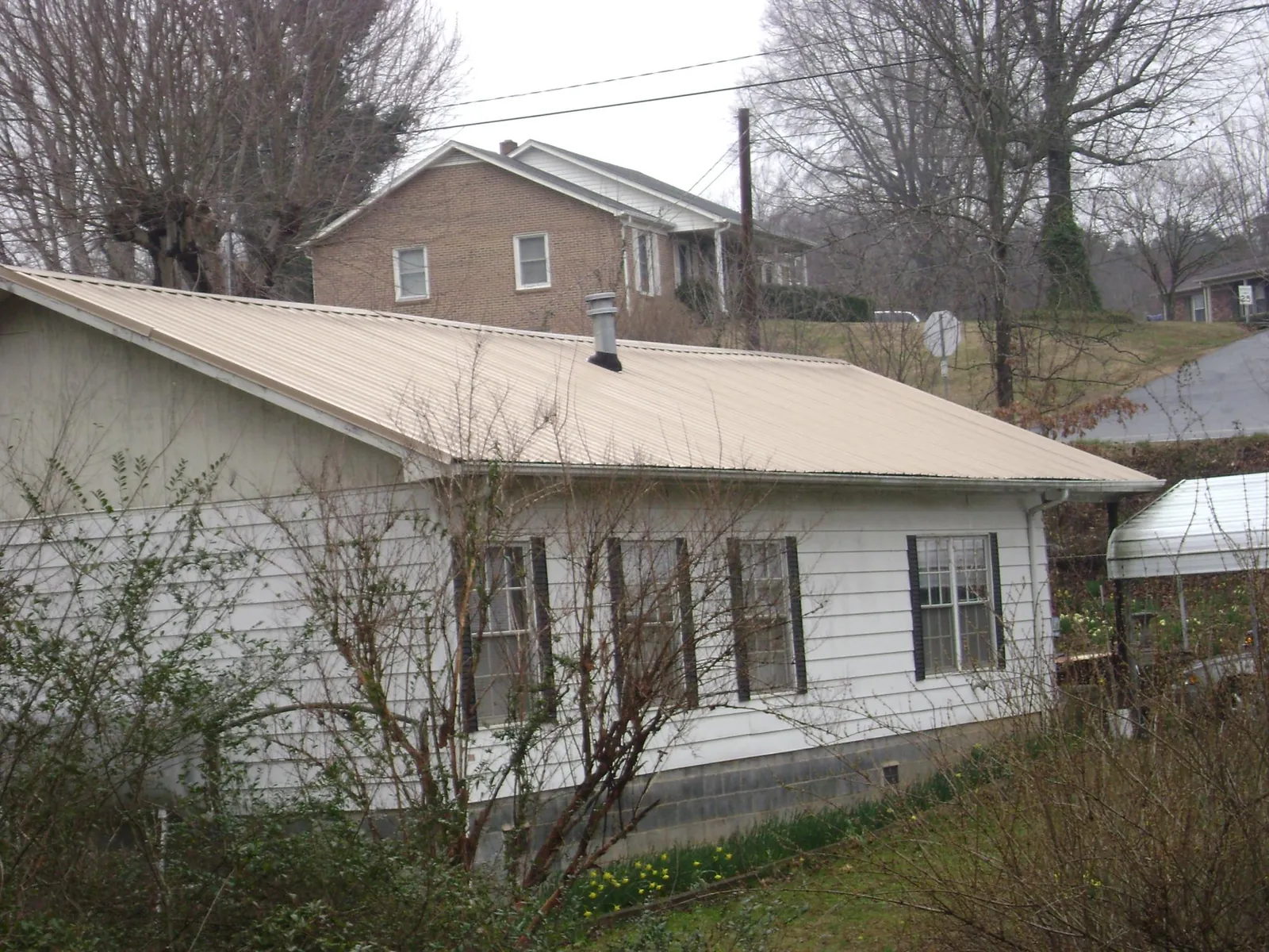 Tan metal roof on a white sided house set into a hillside — Commercial Roofing by Roofing Brothers in Greenwich